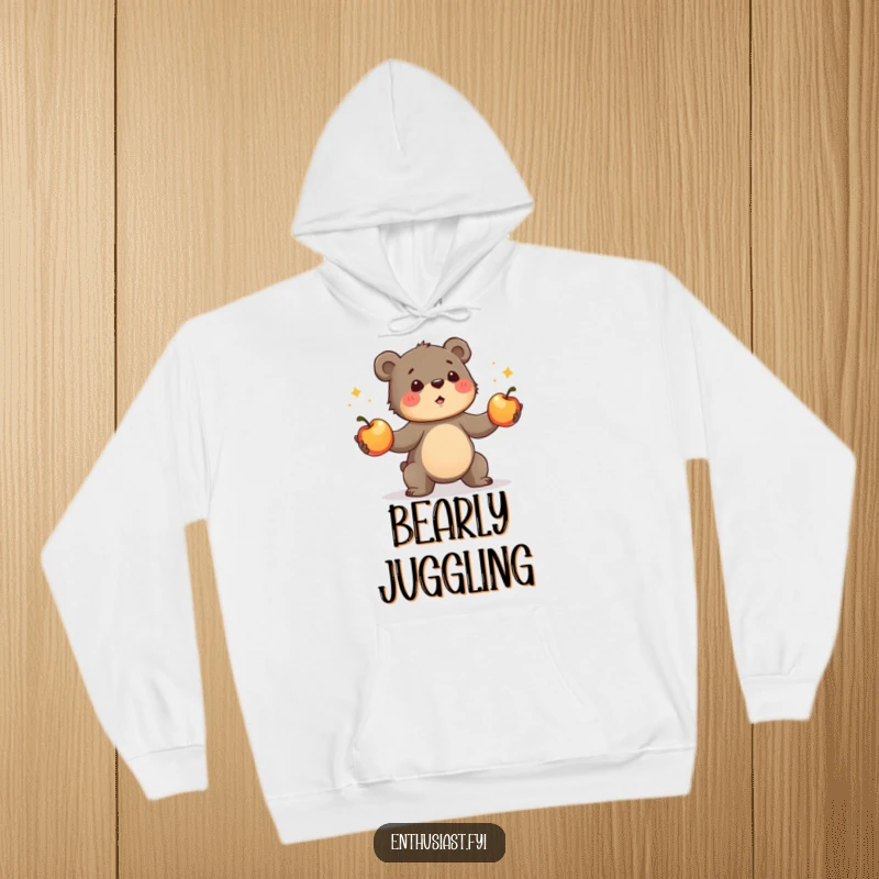 Funny bear cub hoodie, showing a determined cub enthusiastically juggling shiny apples. A cozy and humorous apparel gift.